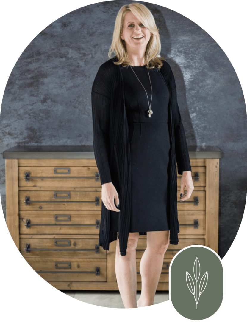 A woman in black dress standing next to a dresser.